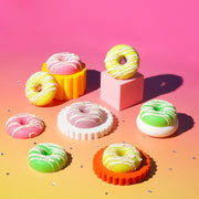 Colorful donuts with icing displayed on pastel geometric stands against a pink gradient background